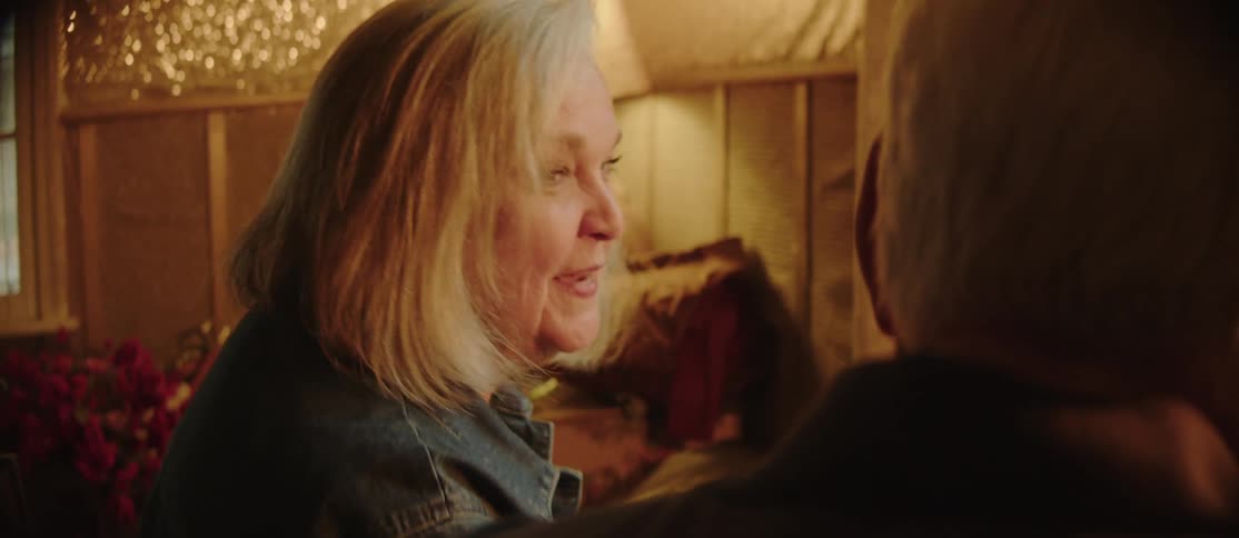 Smiling elderly woman sitting talking to another elderly man next to her