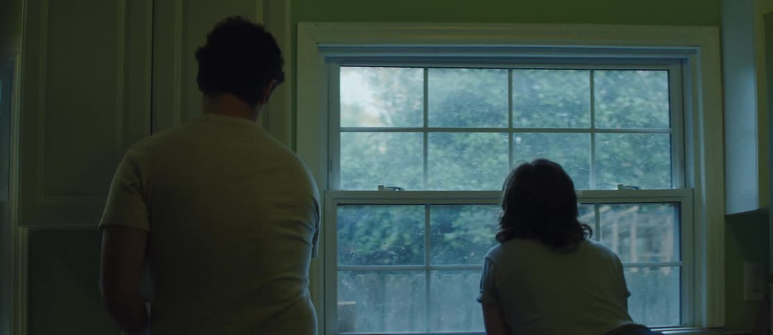 Man getting a coffee and kissing a woman who is facing a window in the kitchen