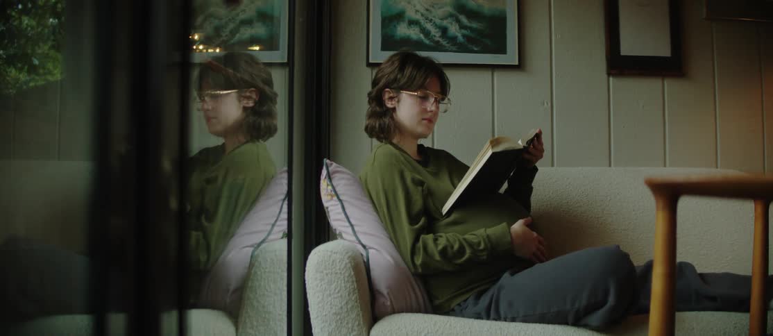 A young pregnant woman is reading a book while reclined on a couch at home
