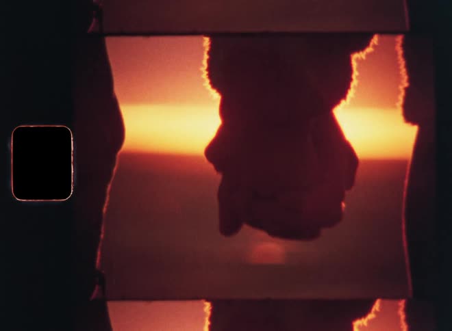 Close up of two people holding hands with the sun on the horizon