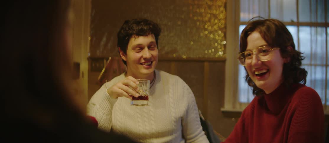 A couple are sitting at a table in a warmly lit room having a conversation and laughing