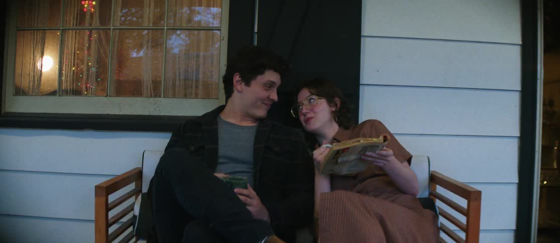 Couple sitting on a bench with the man drinking from a mug and the woman reading a book