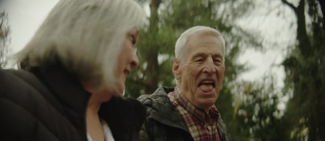 An elderly man and woman trek through the woods