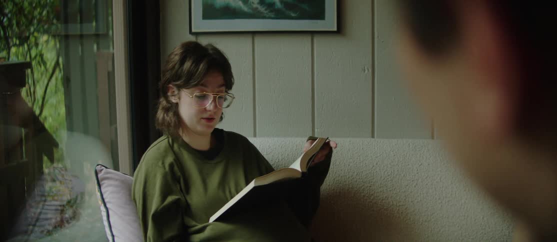 Woman sitting reading a book and a man in the foreground drinking from a mug