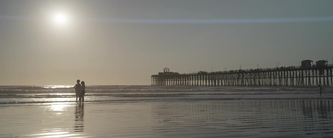Two people on the sand of the beach with the sun on the horizon