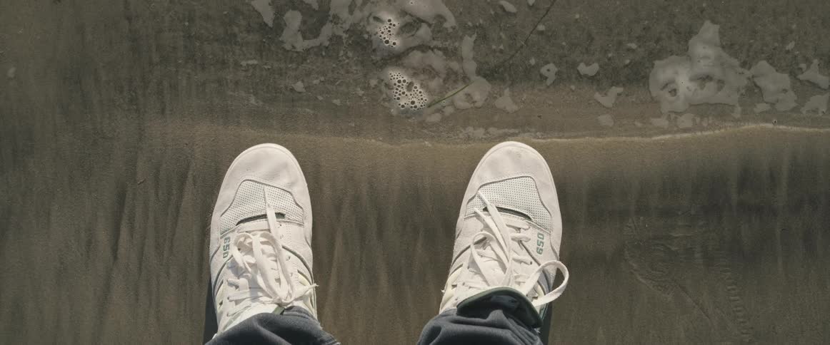 Feet with white sneakers on wet sand
