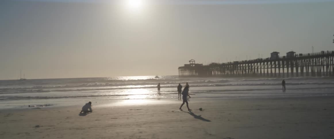 The silhouette of several people on a beach in the morning and there is a huge pier on the right side
