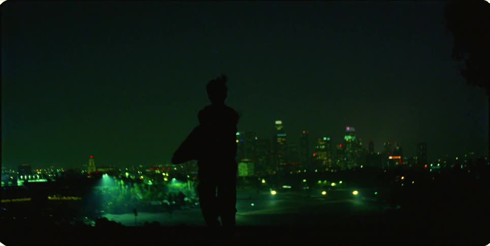 A lone figure dances against a backdrop of a city skyline illuminated with green lights