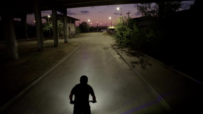 A person rides a motorcycle down a street with an underpass at dusk