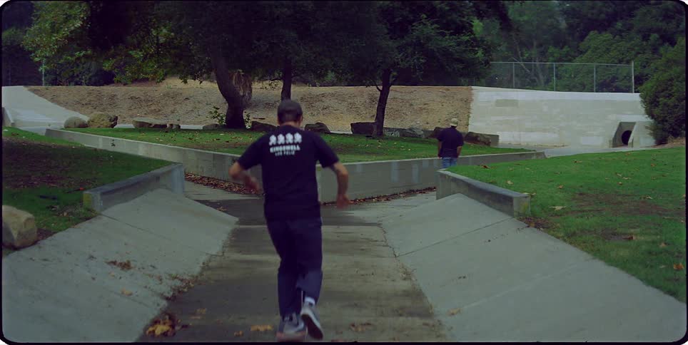 A man pushes off on his skateboard and rides along a sidewalk and up a ramp