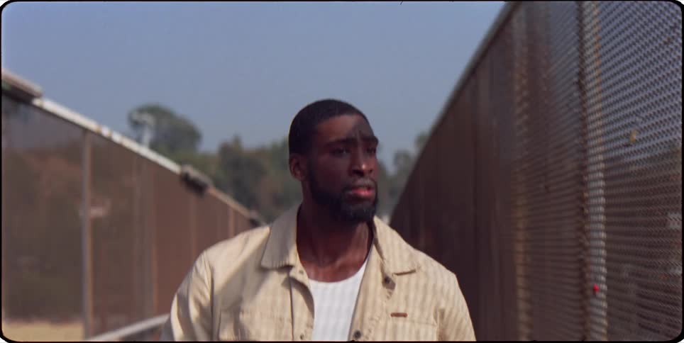A man walks down a narrow path with a fence on each side