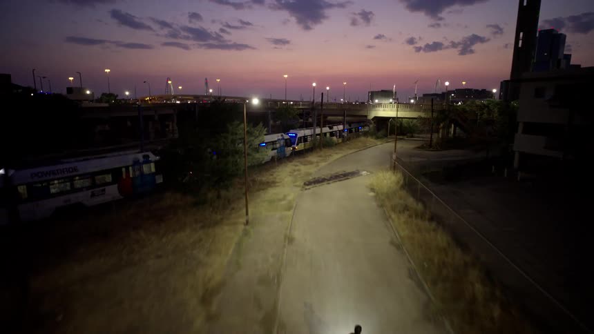 Cyclist riding below an adult next to a train through the city at night