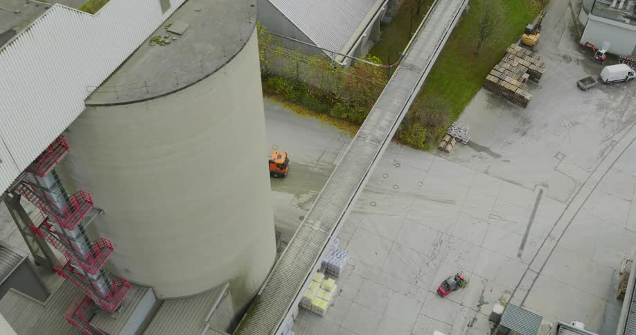 An aerial view of a concrete factory with large silos a raised walkway and trucks transporting materials