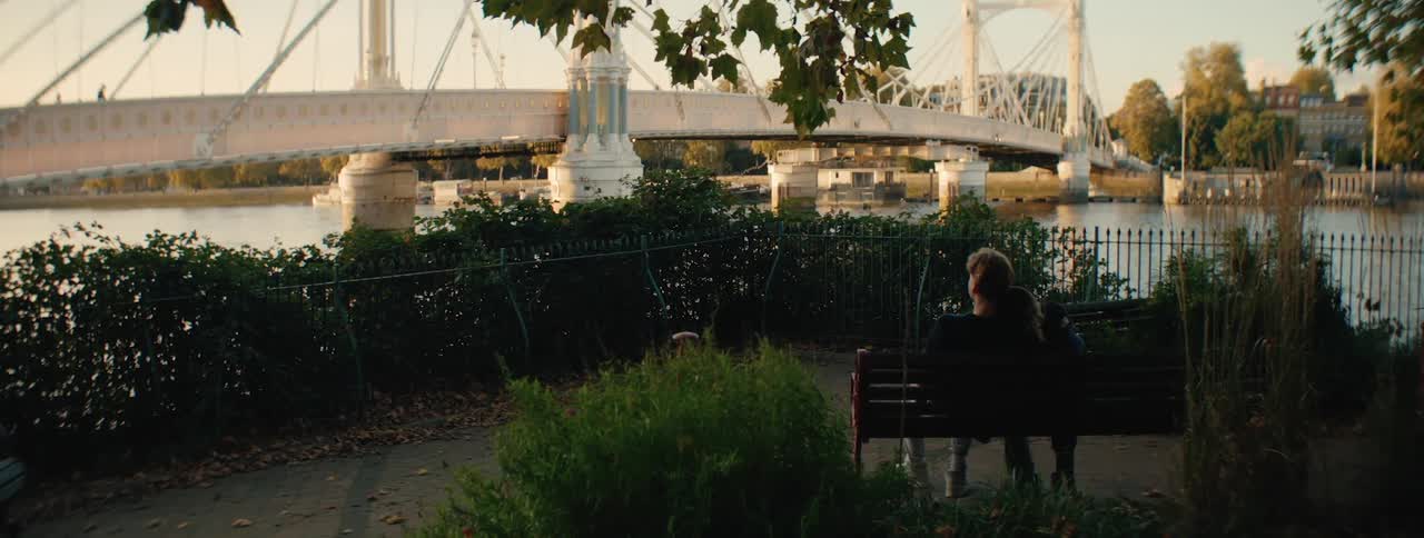 Couple sitting on a park bench facing a lake and a bridge