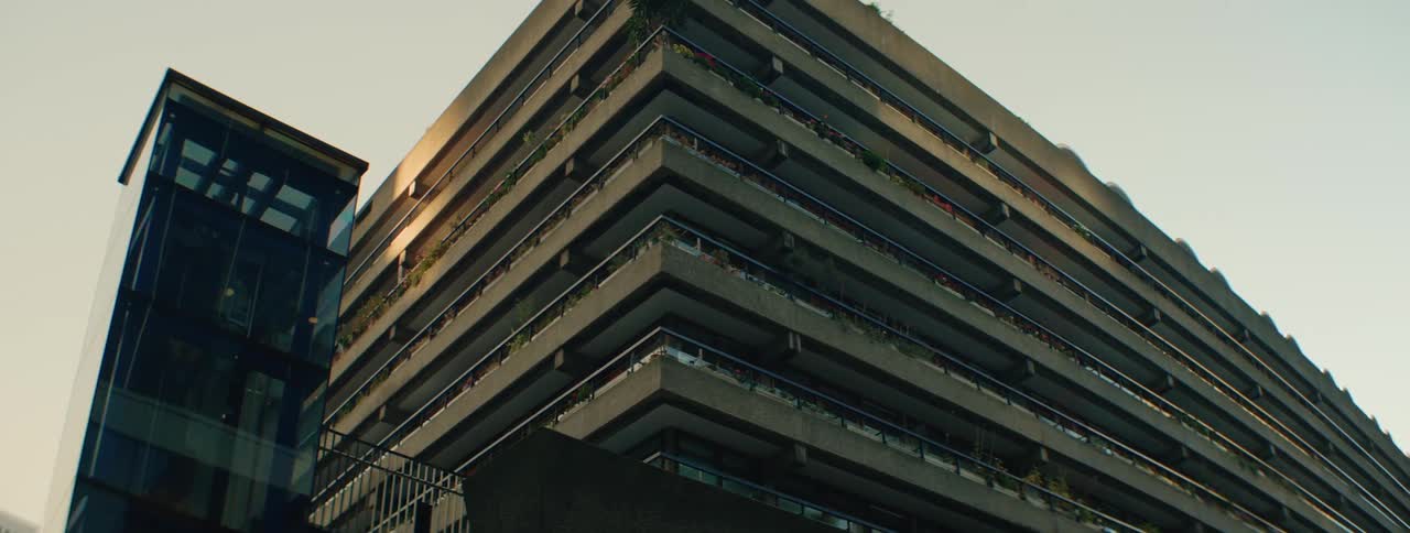 A large imposing concrete building with a glass elevator shaft bathed in the warm glow of the setting sun