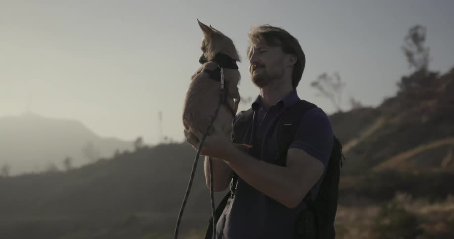 A man holds a chihuahua outside on a sunny day