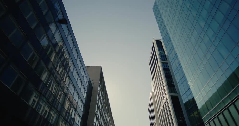 A red double decker bus speeds through a bustling city street dwarfed by the towering skyscrapers that line the road