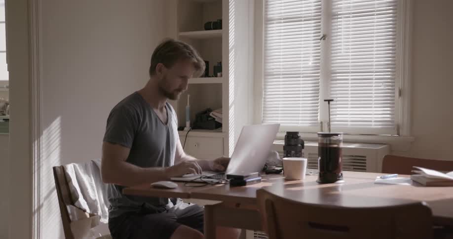 Man types on a laptop at a dining room table