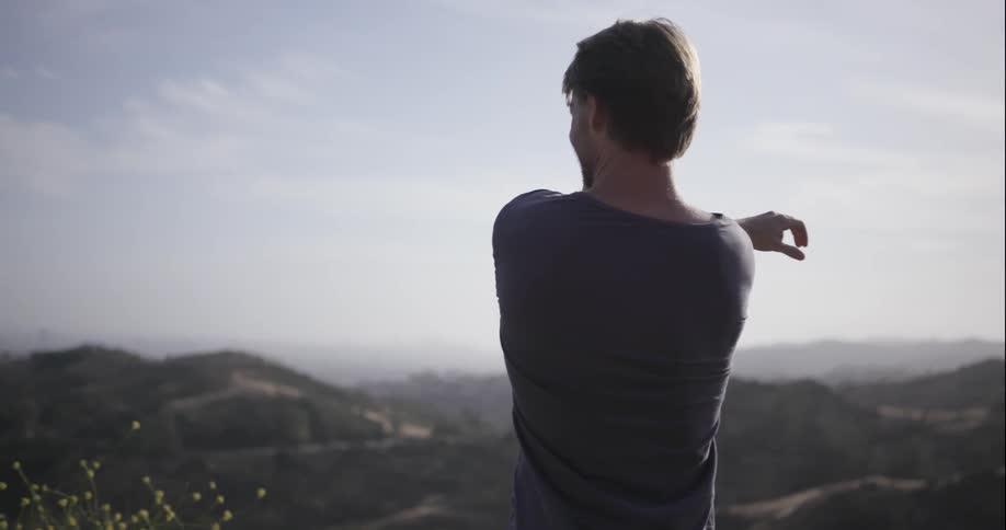 A man is stretching and looking out over an overlook