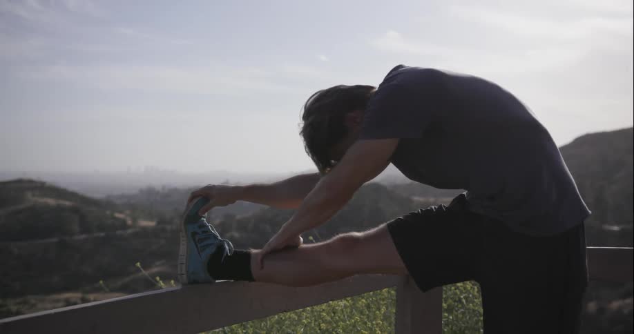 Man stretching his leg with the help of a railing on a partly cloudy day