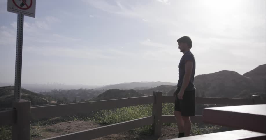 A man stretches his legs on a fence overlooking a valley