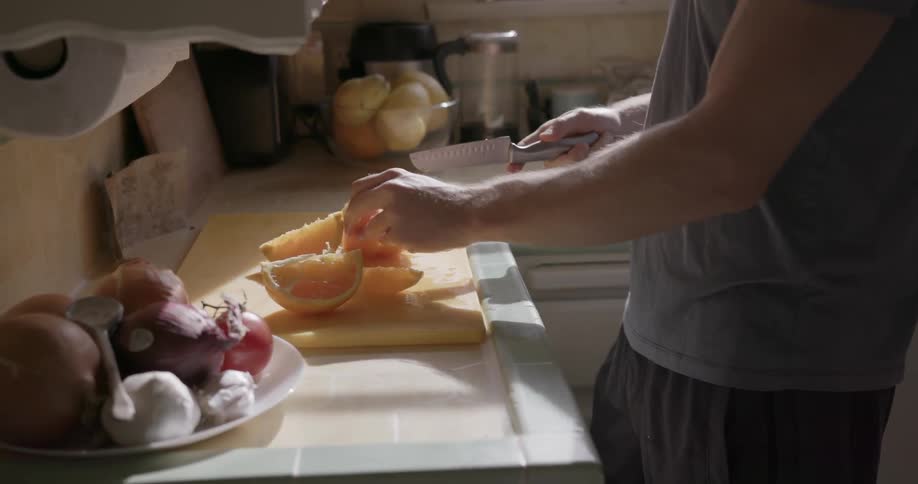 A man cuts an orange in a kitchen