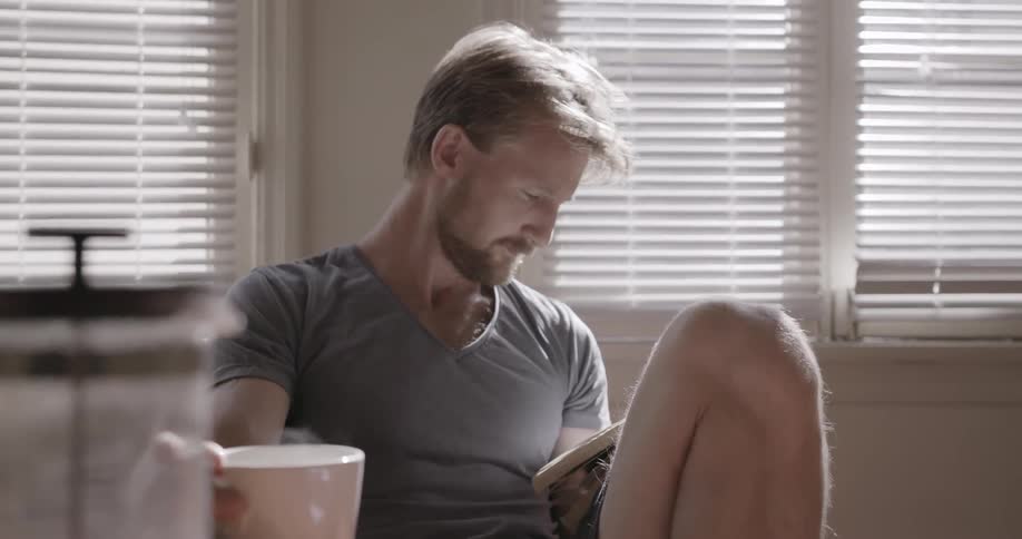 Man looks at a book while drinking coffee at a table