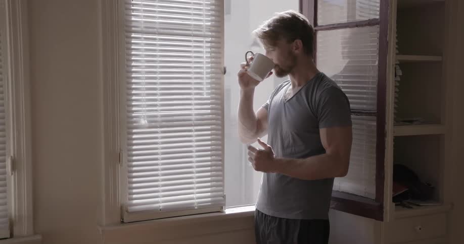 Man takes a drink out of a coffee mug while looking out a window