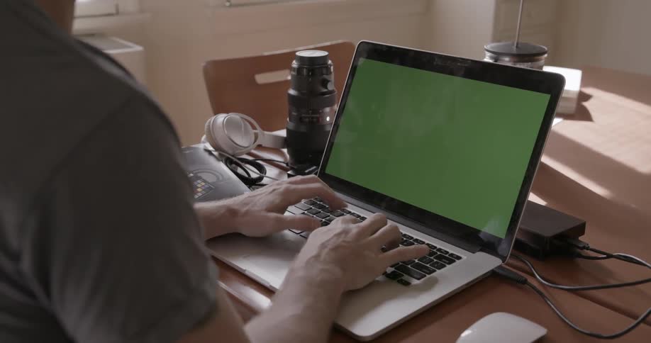 A person types on a laptop with a green screen