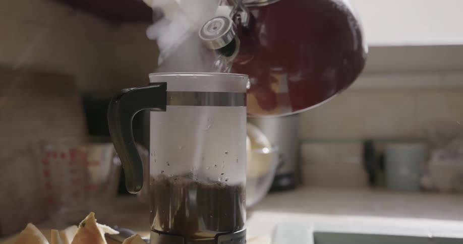 A man picks up a kettle of hot water and pours it into a french press