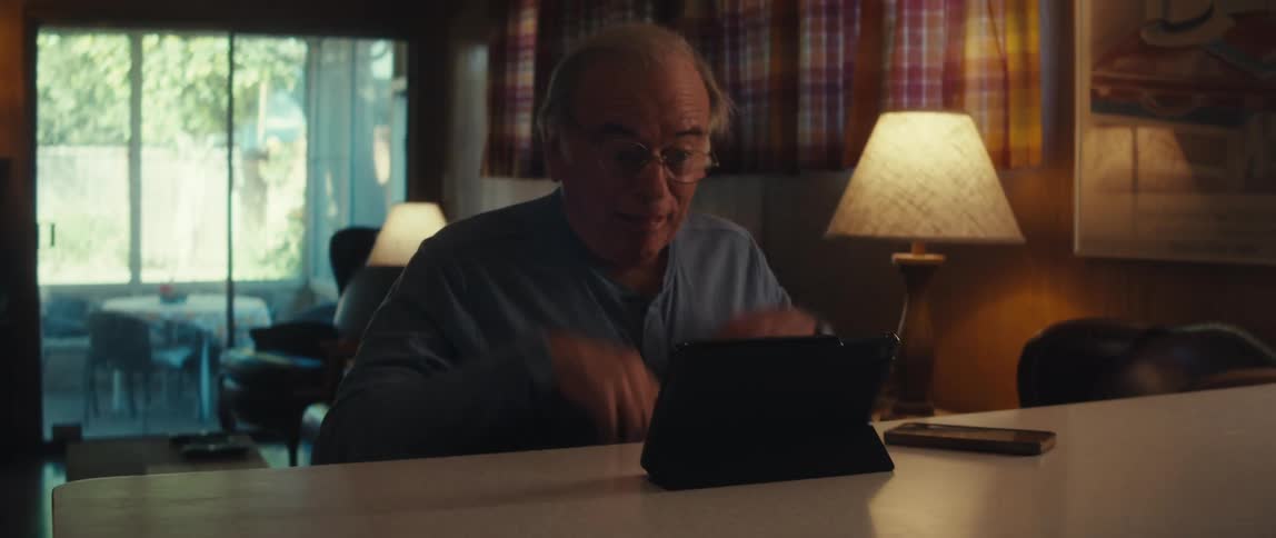 Elderly man sitting grimacing in front of a tablet