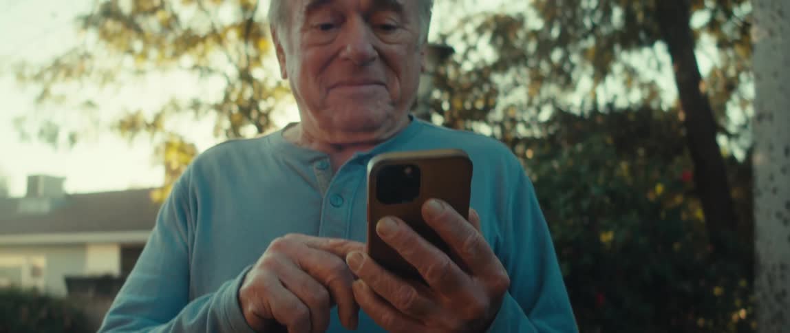 Elderly man in a backyard with trees happily using an iphone