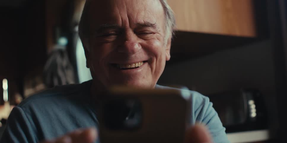 The elderly man uses his smartphone and chuckles in the kitchen