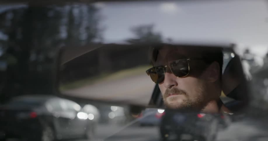 A man driving a car during the day is reflected in his rearview mirror
