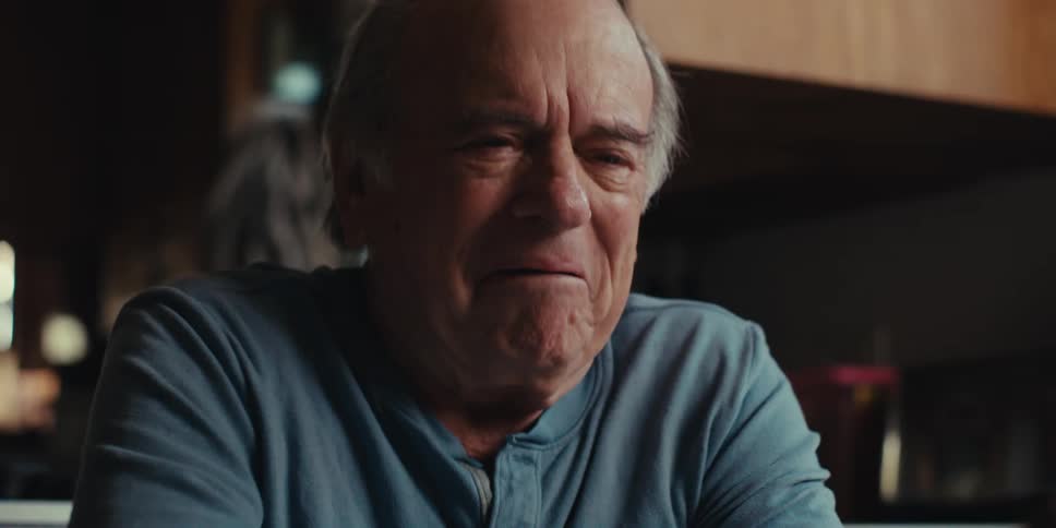 An elderly man is laughing while looking at his smartphone