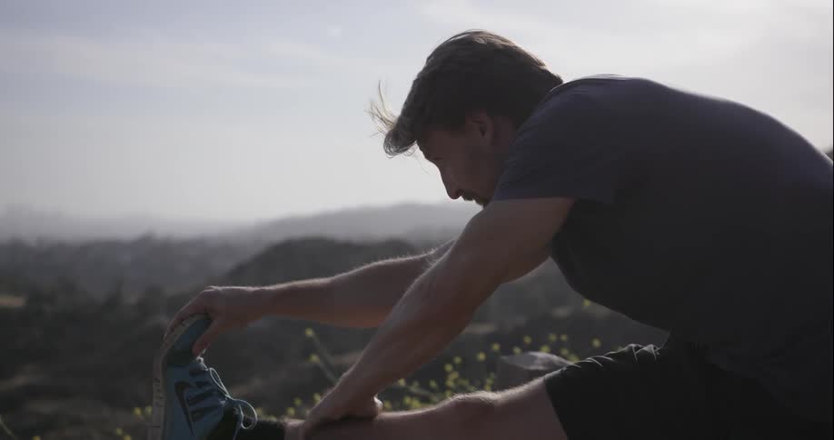 A man stretches his leg while overlooking a valley