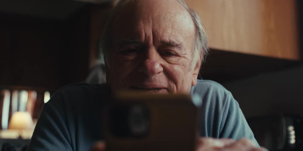 Elderly man with happy facial expression sitting at table and using smartphone