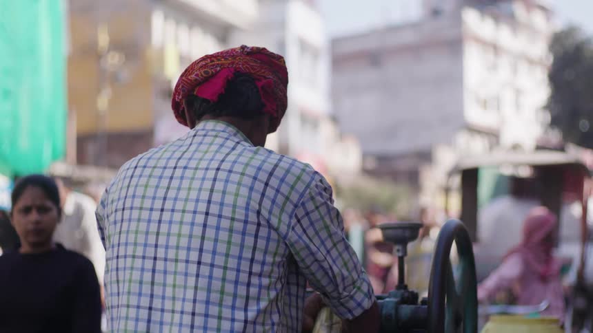 People walking on a street with a man preparing sugarcane juice in a machine