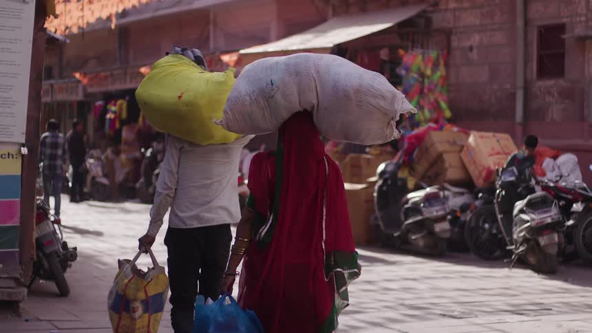 A man and a woman carrying bags on their shoulders and heads through the streets of a third world city