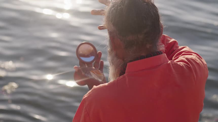 A clip of an elderly man holding a mirror close to the river
