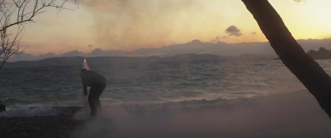 A man launches fireworks on a beach at sunset