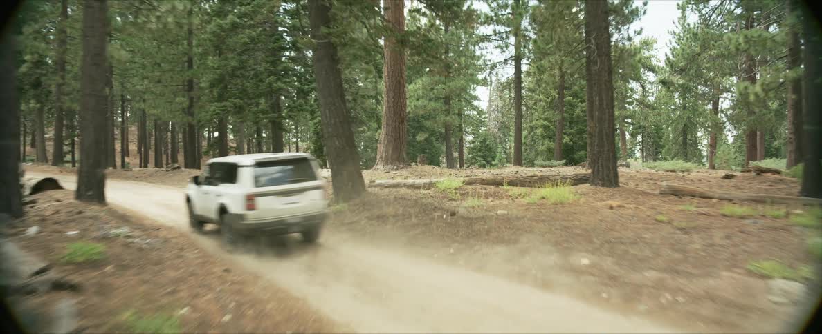 White offroad car traveling along a trail surrounded by conifers
