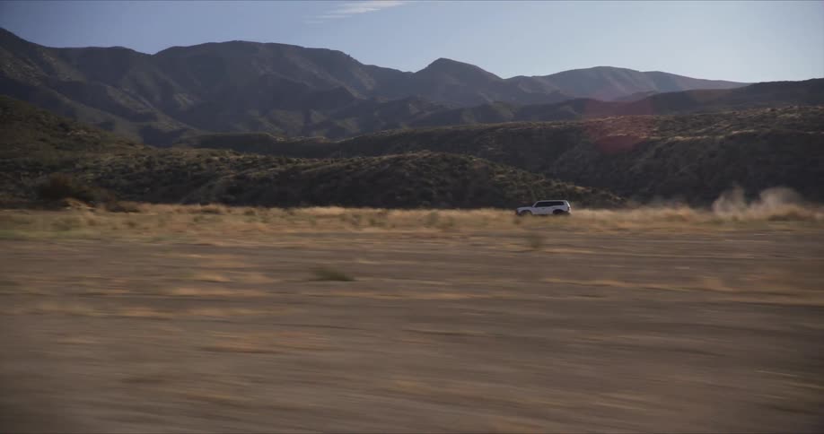 White offroad vehicle speeding down a dirt road with mountains and hills in the background during daytime