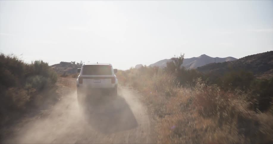 A white suv driving down a dusty dirt road with a scenic mountains in the distance