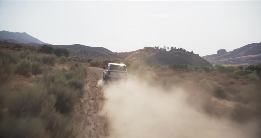 Vehicle driving on dirt trail in a rural area leaving a trail of dust behind