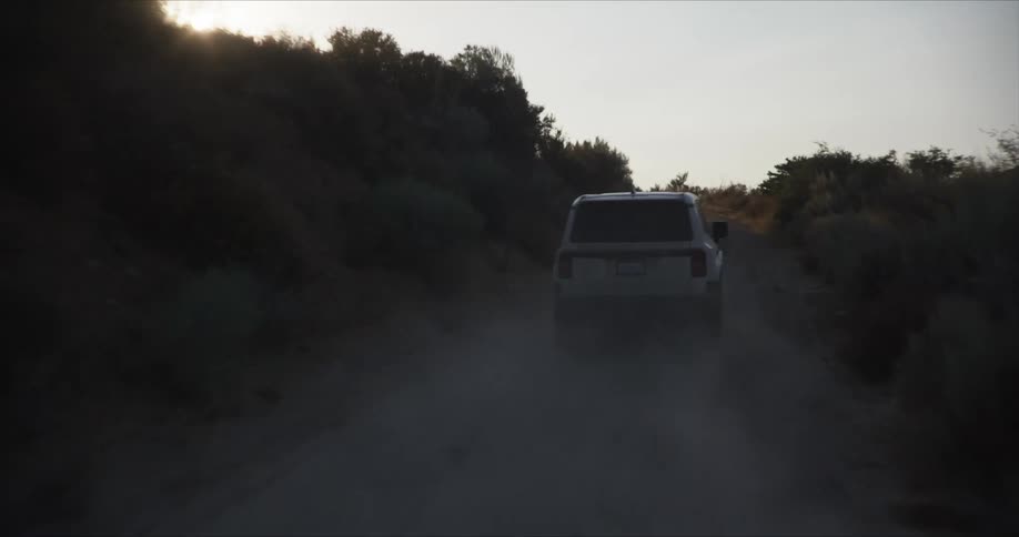 A white suv drives through a winding road bathed in the warm glow of the setting sun