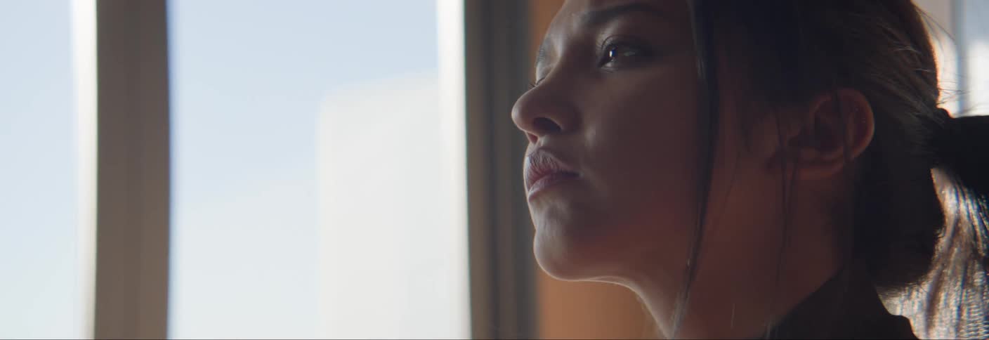 The face of a young woman looking forward and she has her hair tied up and there is a lock of hair on her cheek