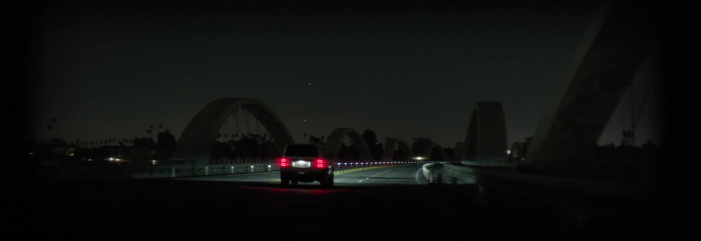 A car drives across a bridge at night its taillights illuminating the dark road ahead