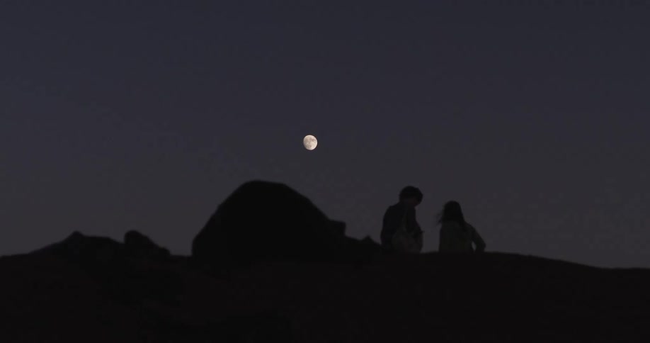 Silhouette of two people at night on a mountain with the moon in the background