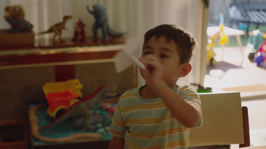 Little boy sitting at table playing with a paper airplane